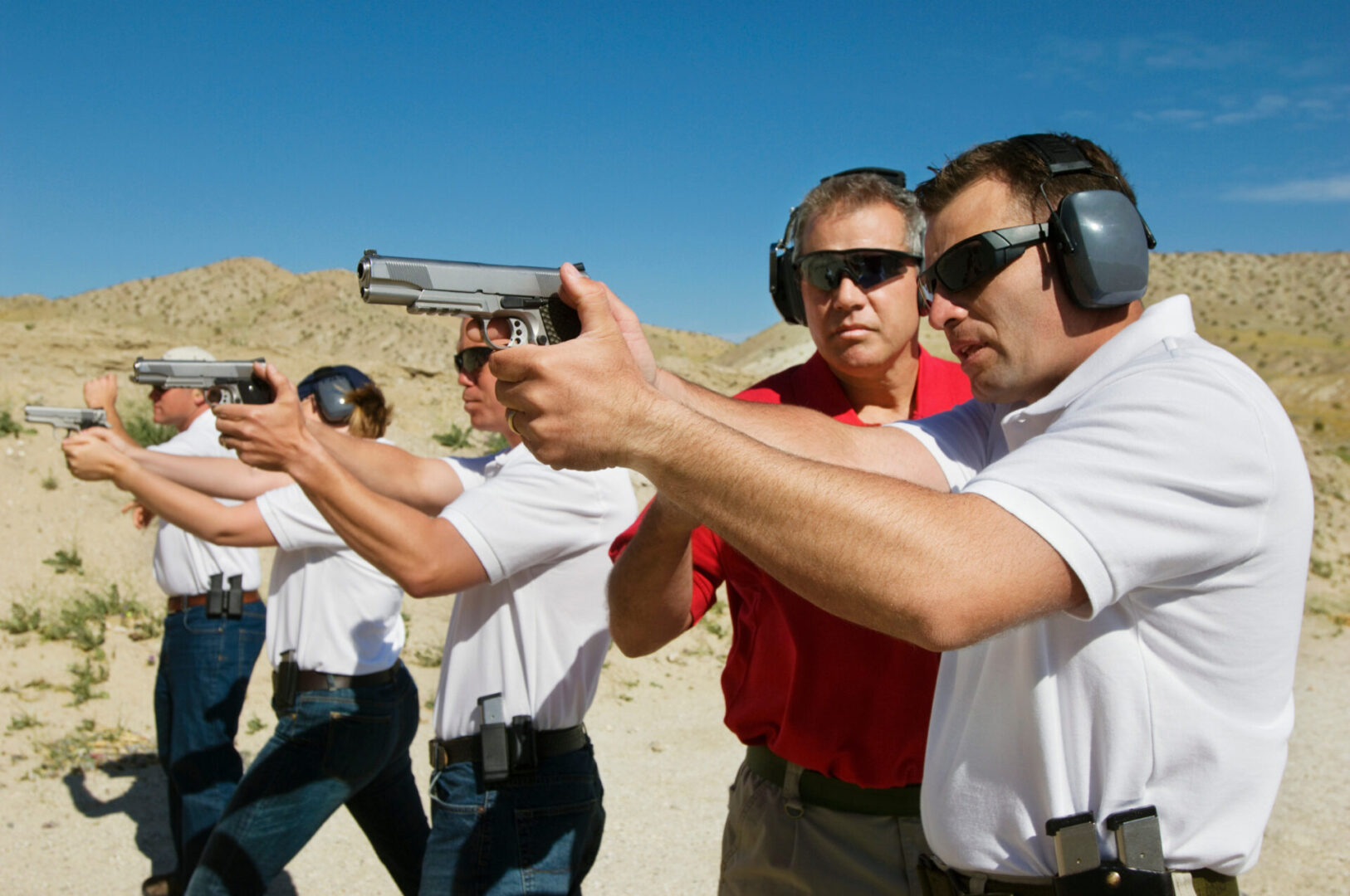 Instructor assisting men aiming hand guns at firing range